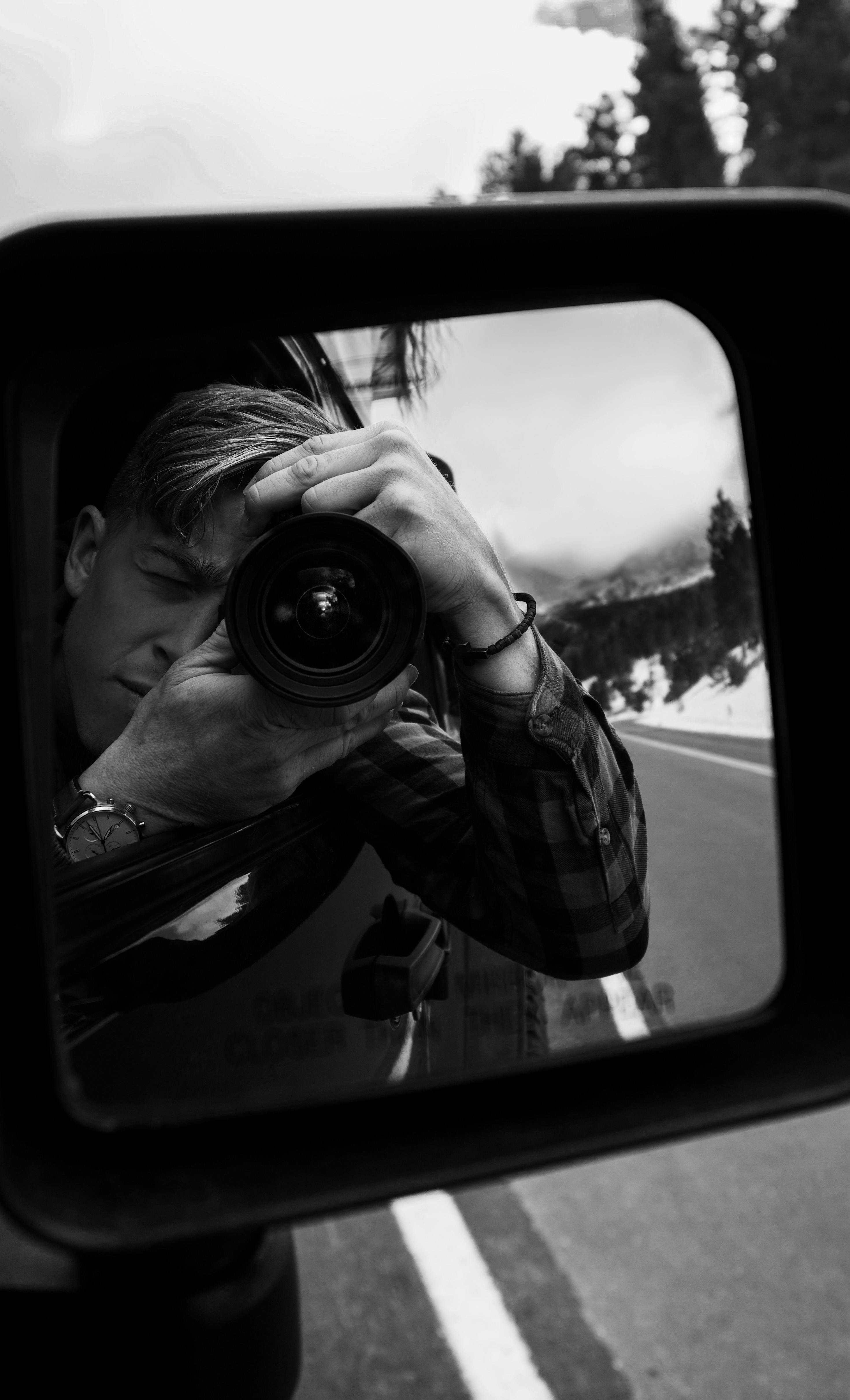 grayscale reflection of man taking photo using dslr camera