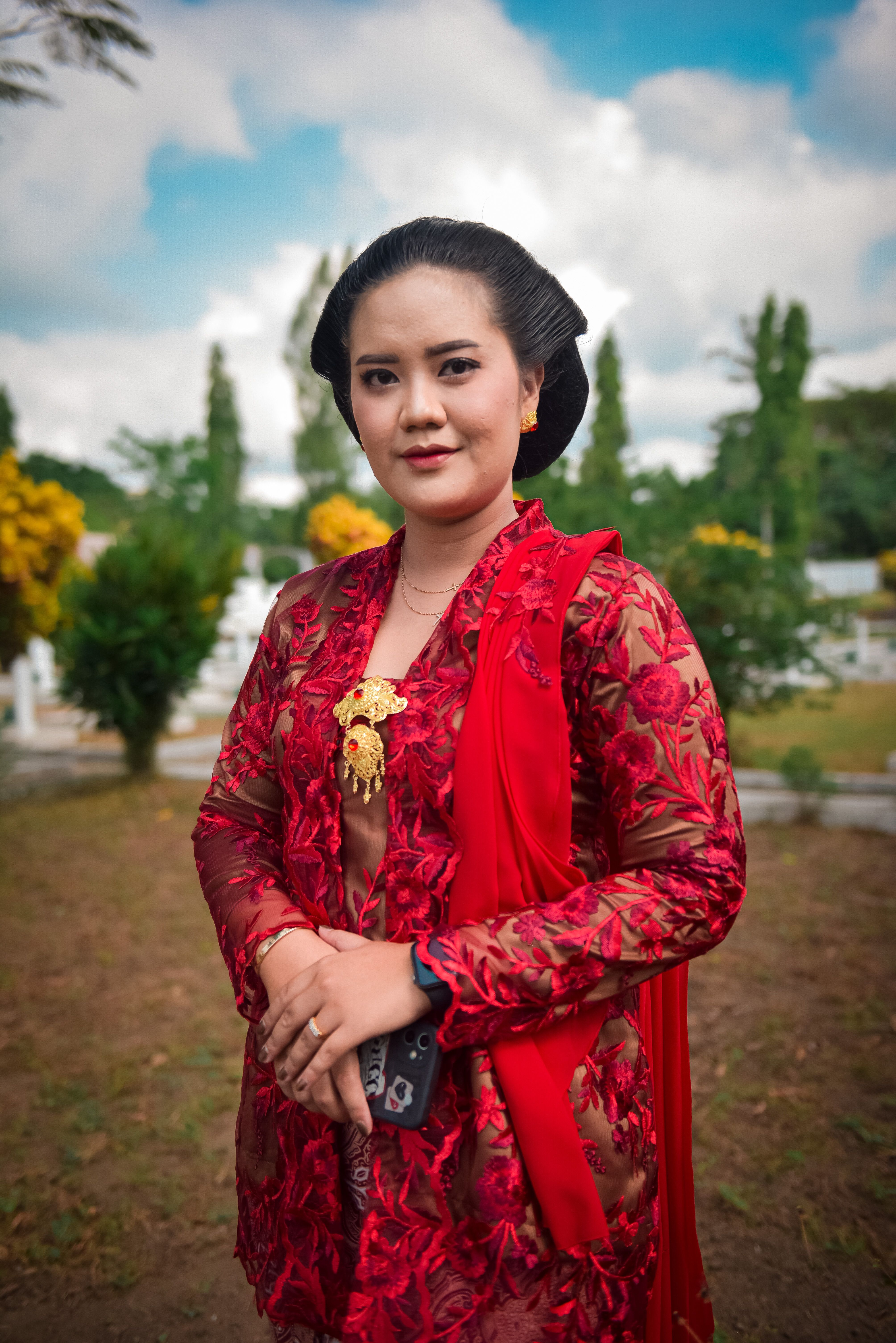 A woman in traditional Indonesian dress poses outdoors, exuding grace and cultural elegance.
