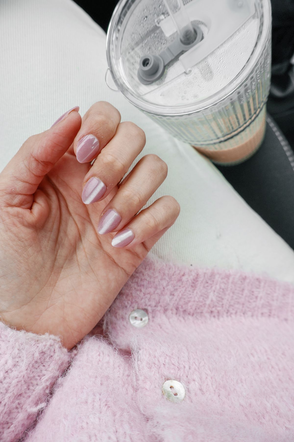 Showcasing pastel pink nails with a cozy sweater and smoothie cup indoors.