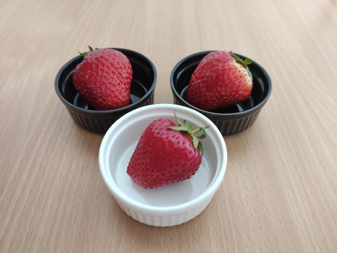 Two black ramekins and one white ramekin each holding a strawberry