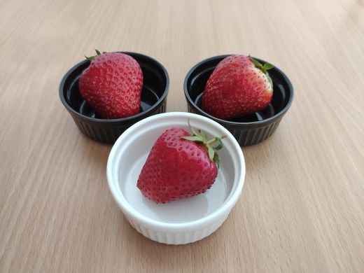 Two black ramekins and one white ramekin each holding a strawberry