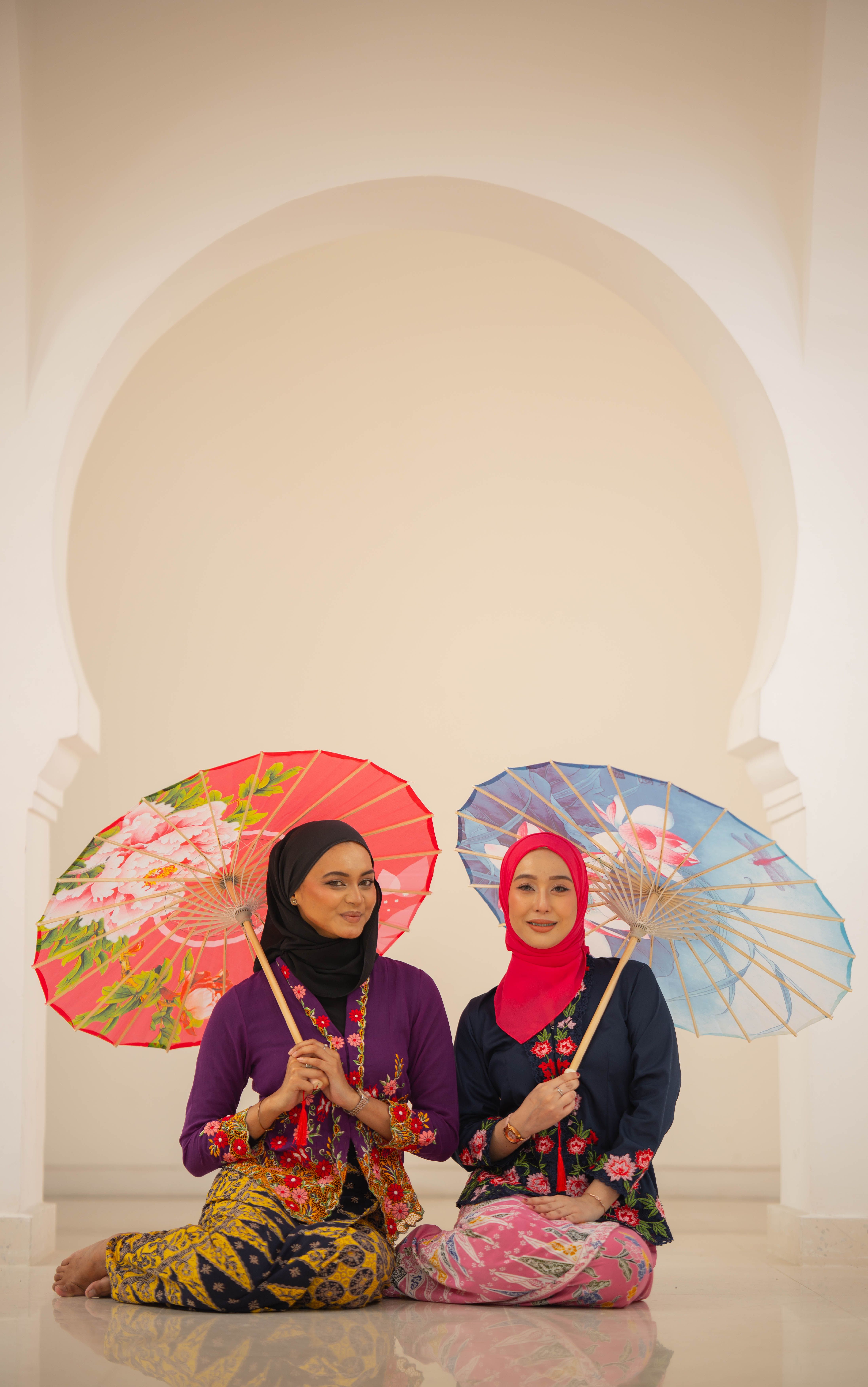Two women in traditional attire holding parasols showcasing cultural elegance indoors.