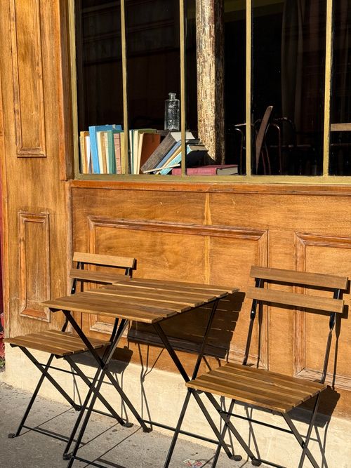 Free Outdoor Parisian cafe scene with wooden chairs, table, and books on a window ledge in sunlight. Stock Photo