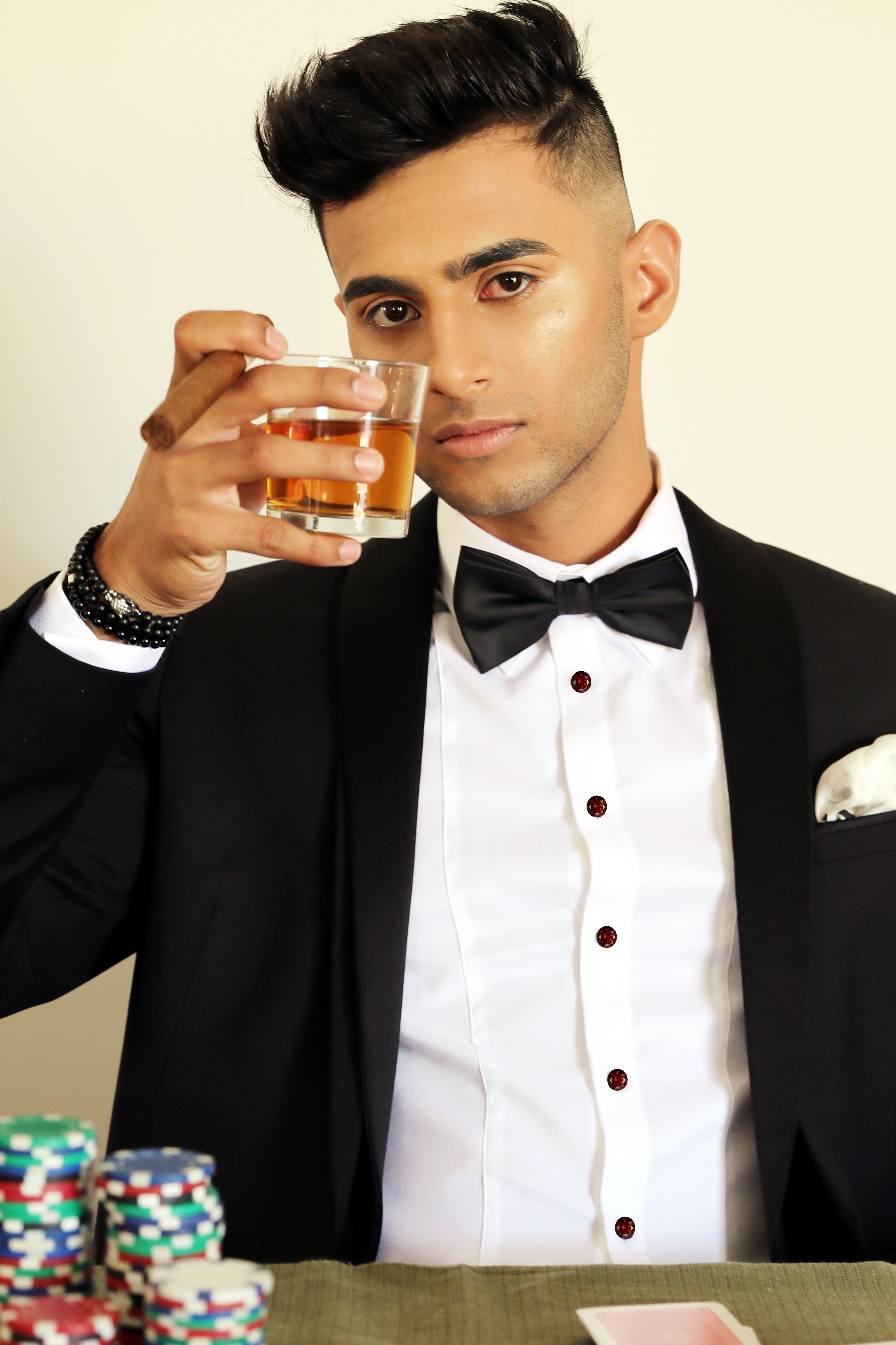 Suave man in tuxedo holds whiskey glass at poker table, showcasing sophistication and style.