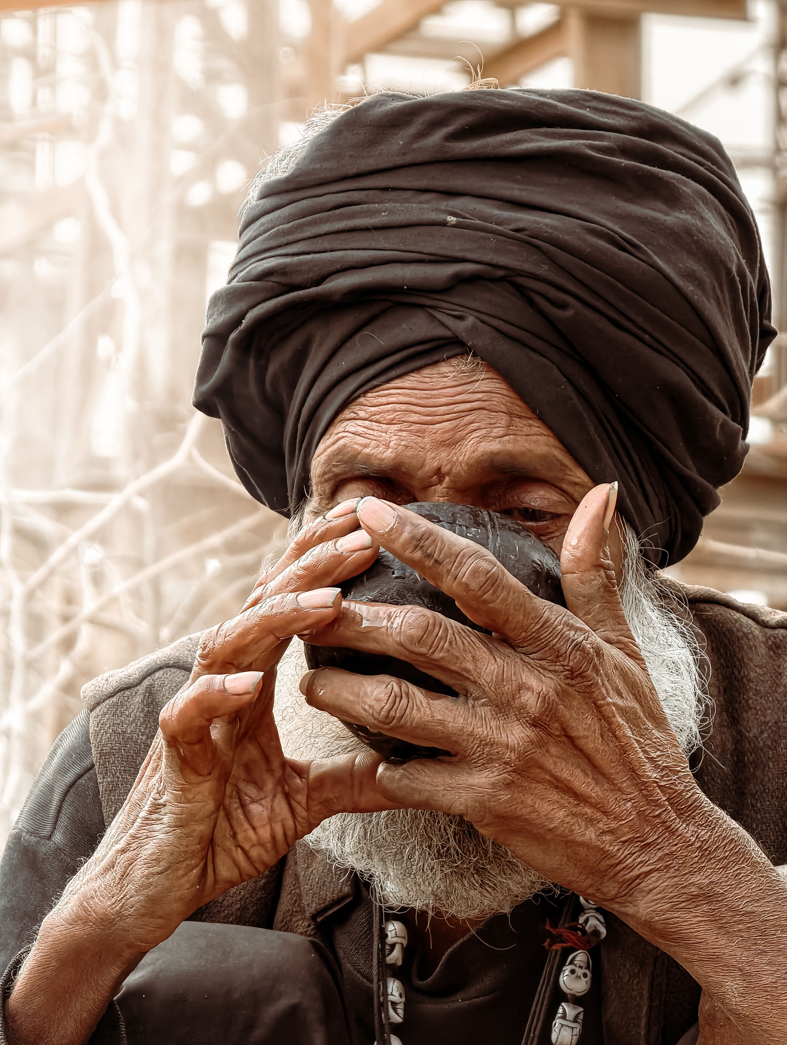 Elderly man in a turban sipping tea, showcasing traditional lifestyle in an outdoor setting. - Health Benefits of Shilajit