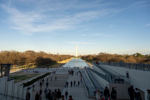 Free View of the Washington Monument and Reflecting Pool with people walking, captured on a sunny day. Stock Photo