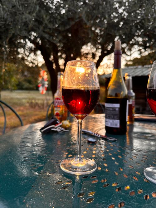 Free A glass of red wine on an outdoor table during sunset, surrounded by nature and evening glow. Stock Photo