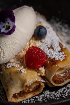 A close-up of freshly made crepes topped with raspberries, blueberries, and a scoop of ice cream.