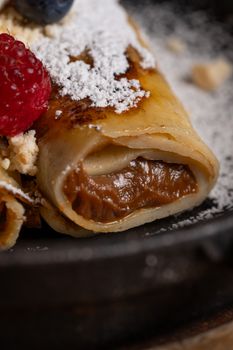 Close-up of a sweet crepe filled with chocolate and topped with powdered sugar and berries.