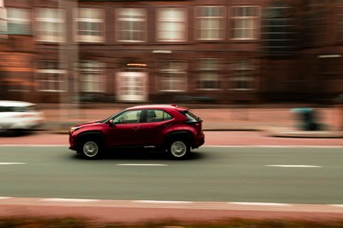 Free Blurred motion shot of a red car speeding through a city street with historic buildings. Stock Photo