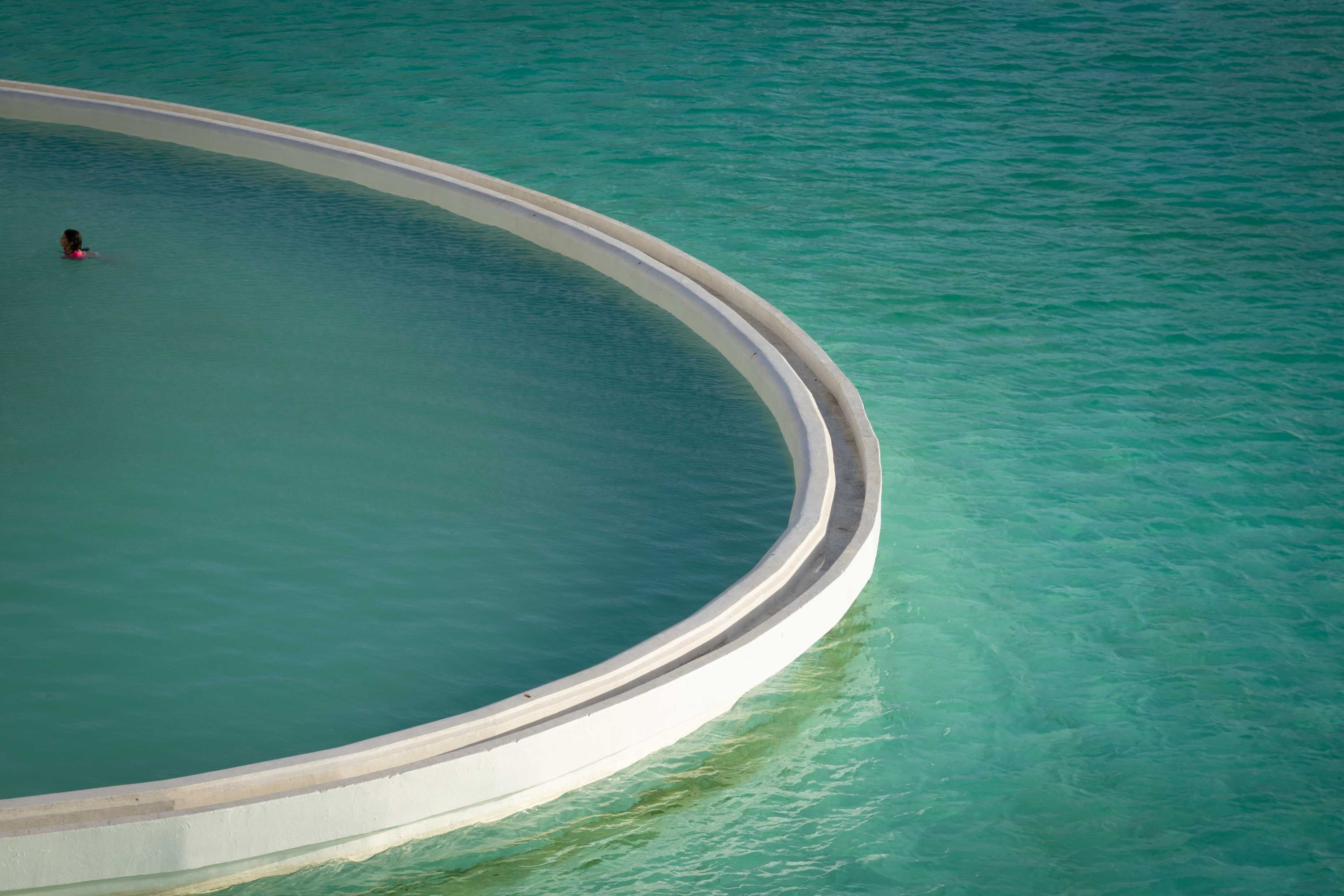 Pessoa nadando em uma piscina infinita curvilínea com vista para o oceano turquesa em um spa de luxo no Chile.