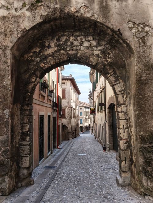 Free Explore a charming European street through a rustic stone archway, revealing historic architecture. Stock Photo
