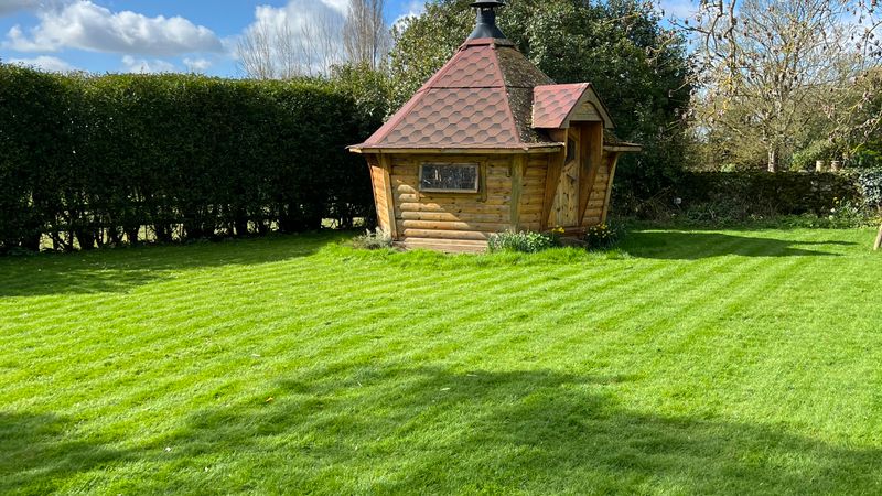 A small timber cabin with a pointed roof on a striped lawn