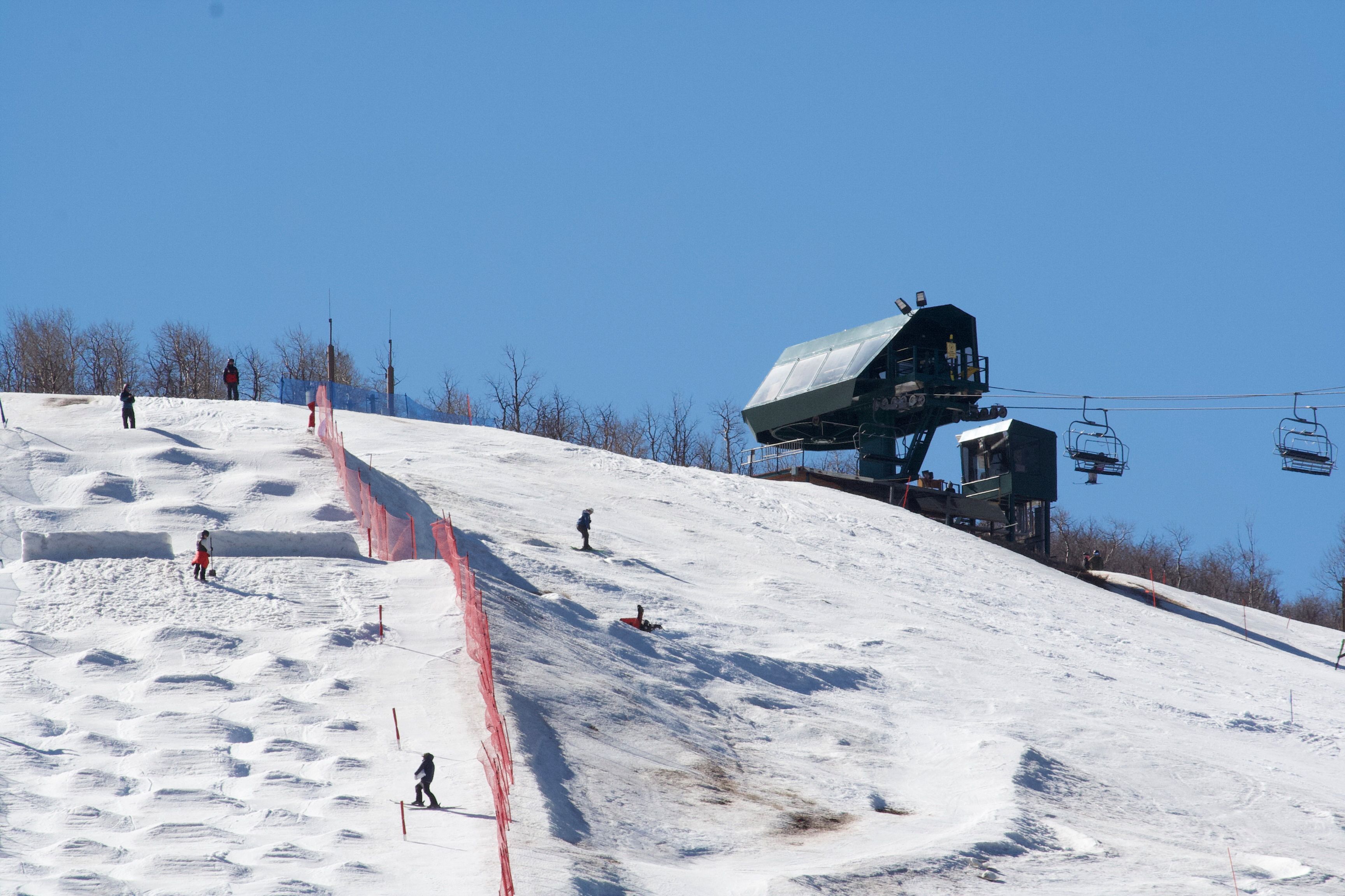 Skiers enjoying a sunny day on snowy slopes with a chairlift in the background.