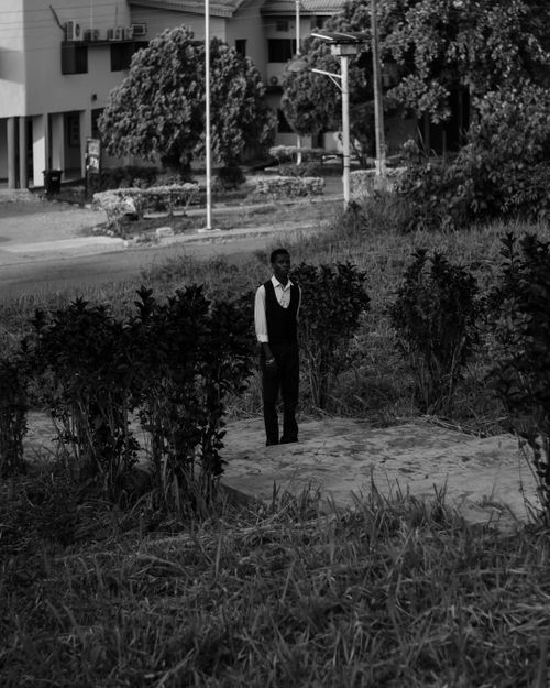 Free Black and white image of a solitary man standing amidst urban greenery, exuding a moody and classic atmosphere. Stock Photo