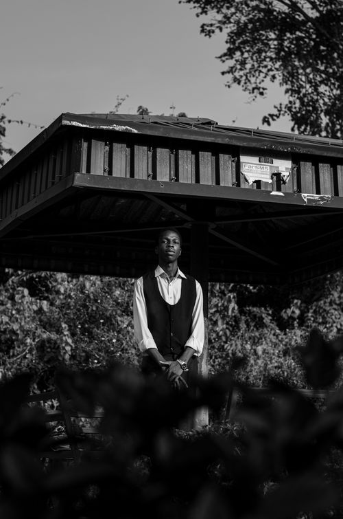 Free Black and white portrait of a man standing in a gazebo, surrounded by foliage. Stock Photo