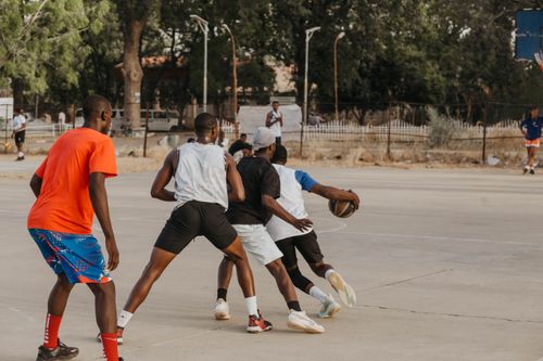 Free Group of young men playing basketball on an outdoor court in a lively match. Stock Photo