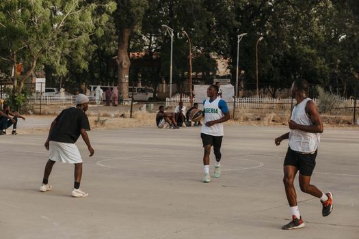 Young men playing a basketball game outdoors on a sunny day in a park setting, showcasing athleticism and teamwork.