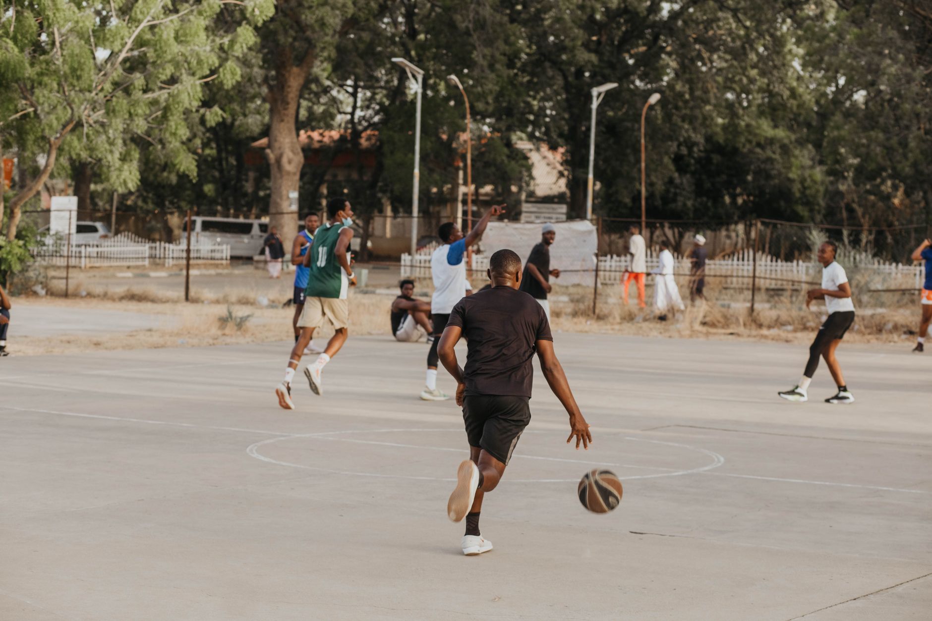 Players enjoy a basketball game on an outdoor court surrounded by trees.