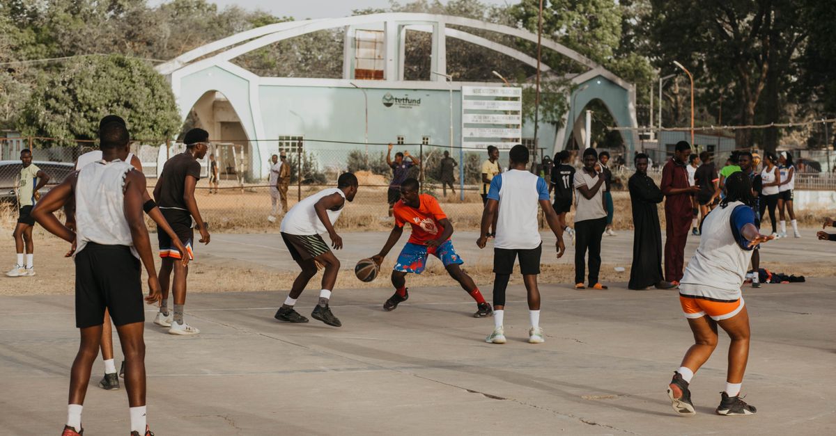 Local children and teenagers playing basketball on an outdoor court at Loveworld Arena in Barracks Newtown, Ho, Ghana