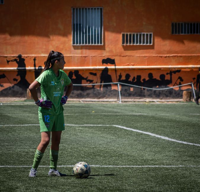 Young female soccer player standing on a field ready to kick the ball during a match.