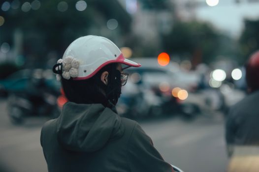 A person wearing a helmet and mask observing traffic in an urban setting during twilight.