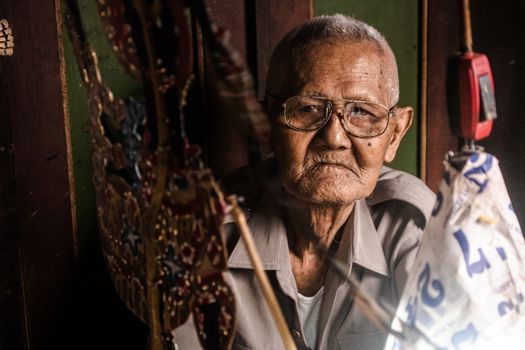 Portrait of an elderly man in Yogyakarta, Indonesia, with traditional Wayang puppets, reflecting cultural heritage.