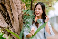 Smiling Woman Outdoors by Tree Holding Flower
