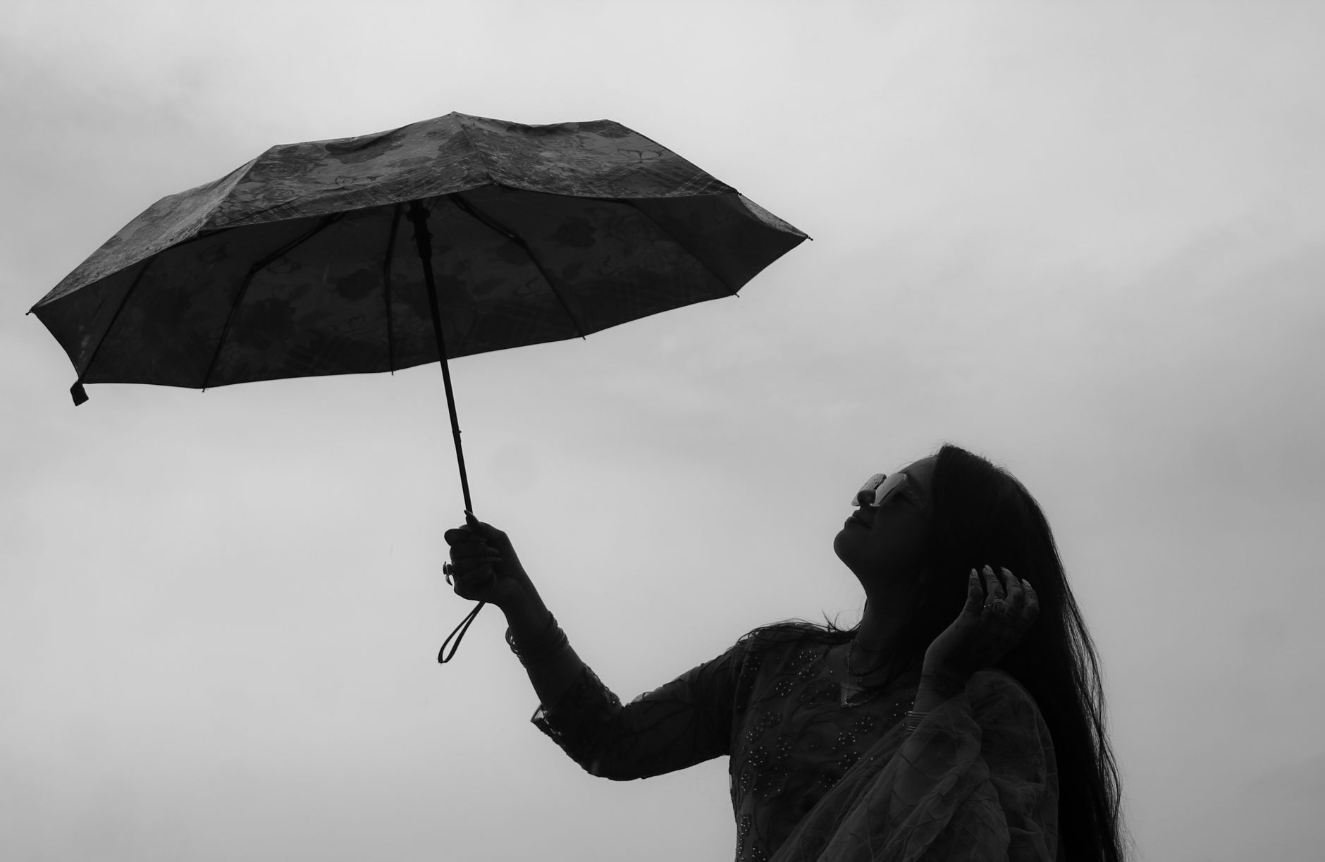 Monochrome silhouette of a woman holding an umbrella against a cloudy sky, evoking themes of elegance and solitude.