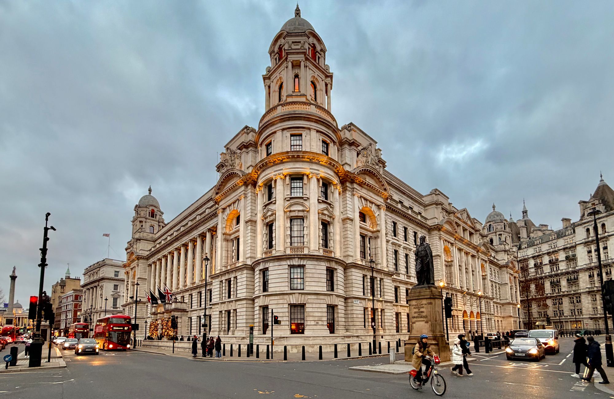 A bustling street scene featuring a grand Edwardian building in Central London at dusk, showcasing urban life.