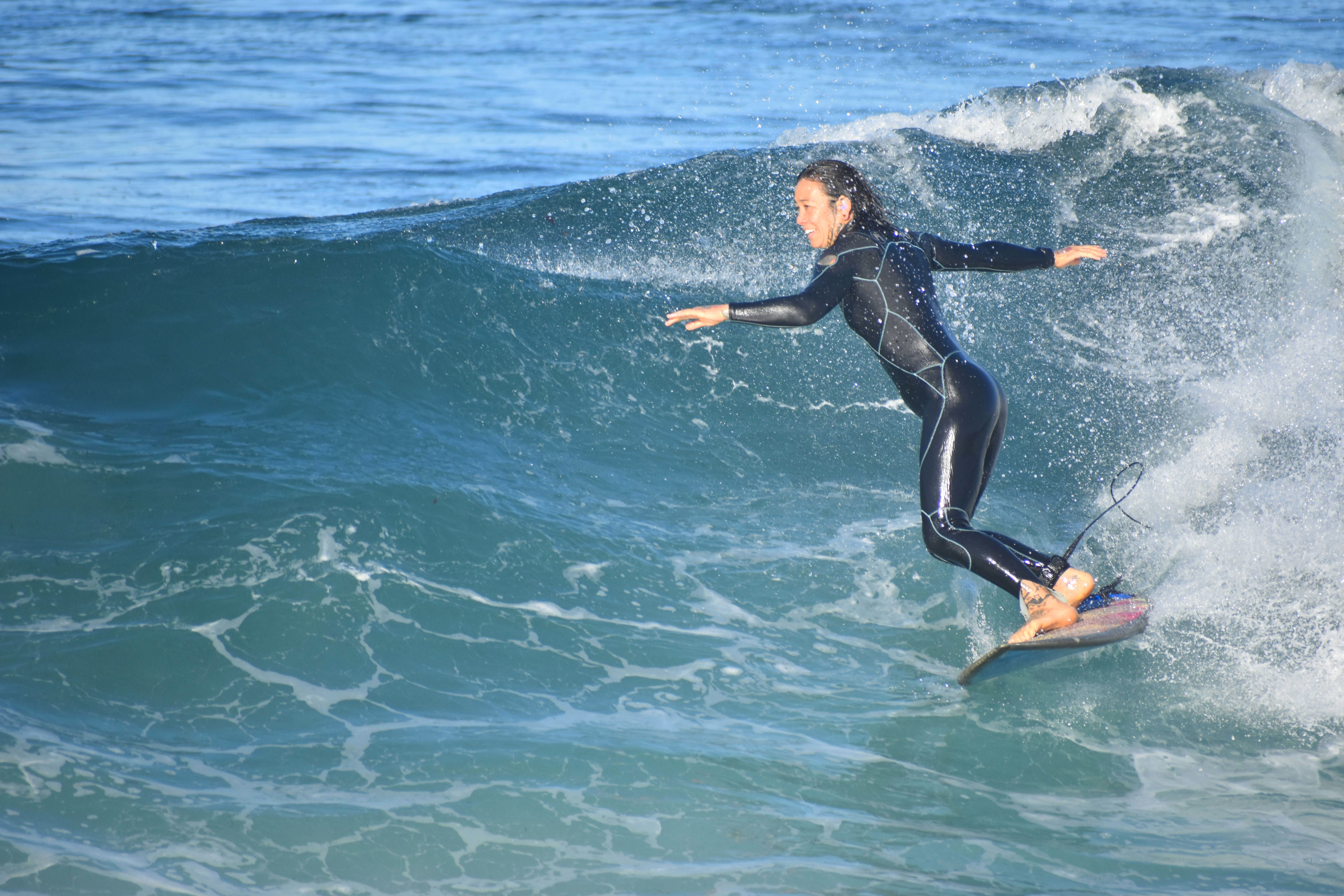 Woman in wetsuit skillfully surfs a large ocean wave, showcasing her surfing ability.