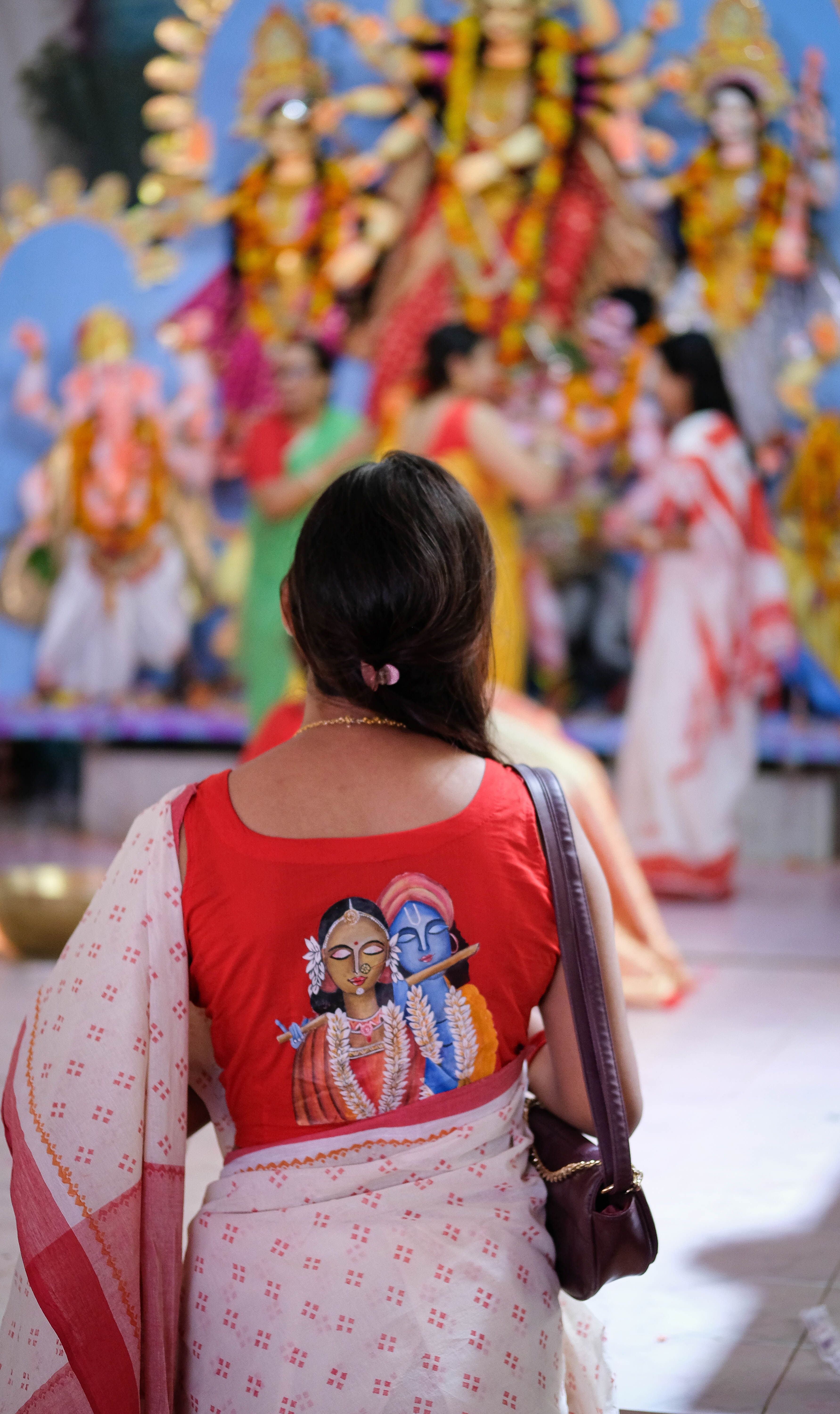 A woman in traditional attire observes vibrant religious festival with colorful deities.