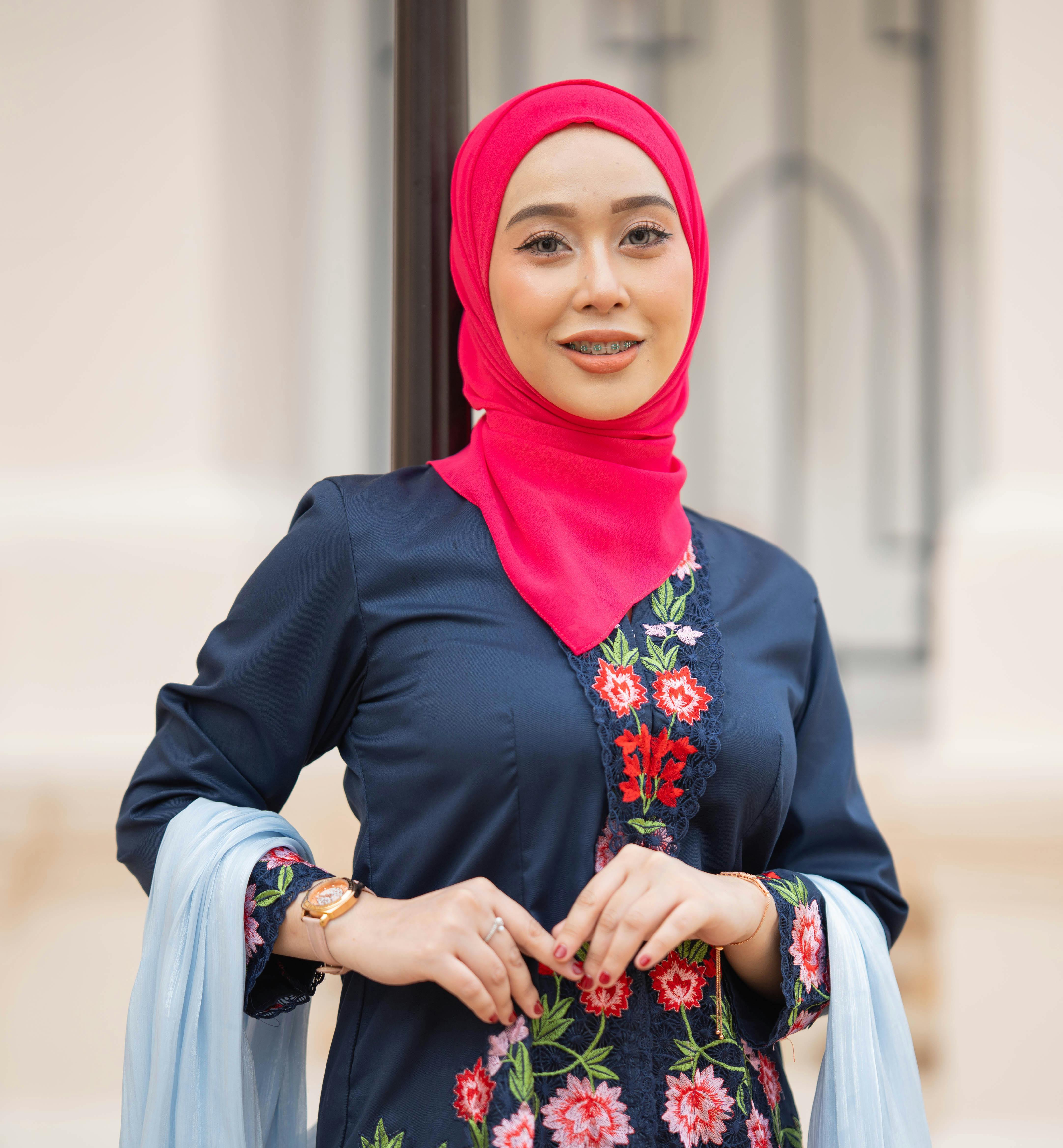 Portrait of a smiling woman wearing a red hijab and embroidered traditional dress outdoors.