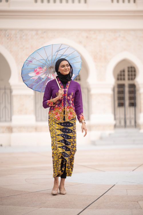 Free A woman in vibrant traditional attire stands outdoors holding a floral parasol in an elegant setting. Stock Photo