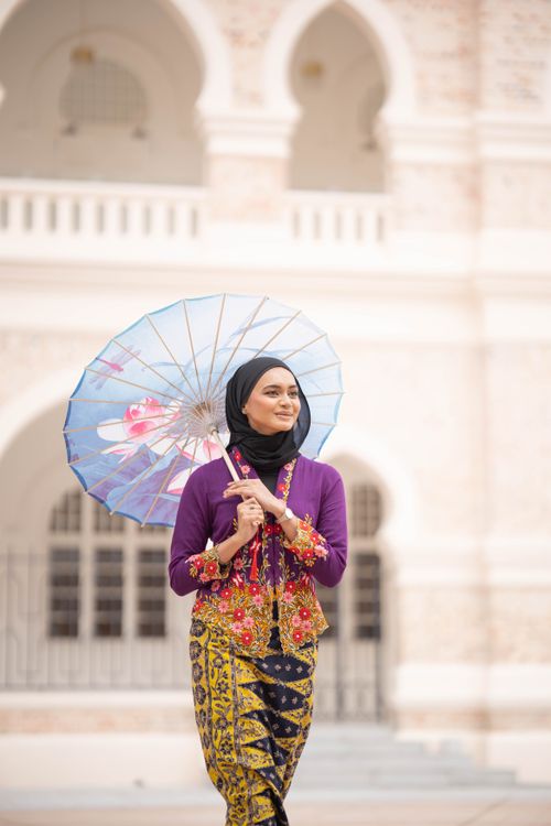 Free A stylish woman in traditional attire holding a parasol, standing before a historic building. Stock Photo
