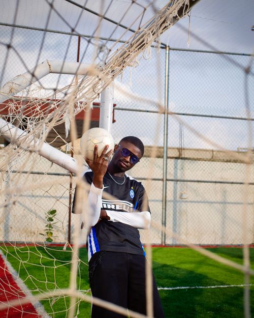 Free Stylish young man poses confidently in a soccer net with a ball, showcasing a vibrant sports vibe. Stock Photo