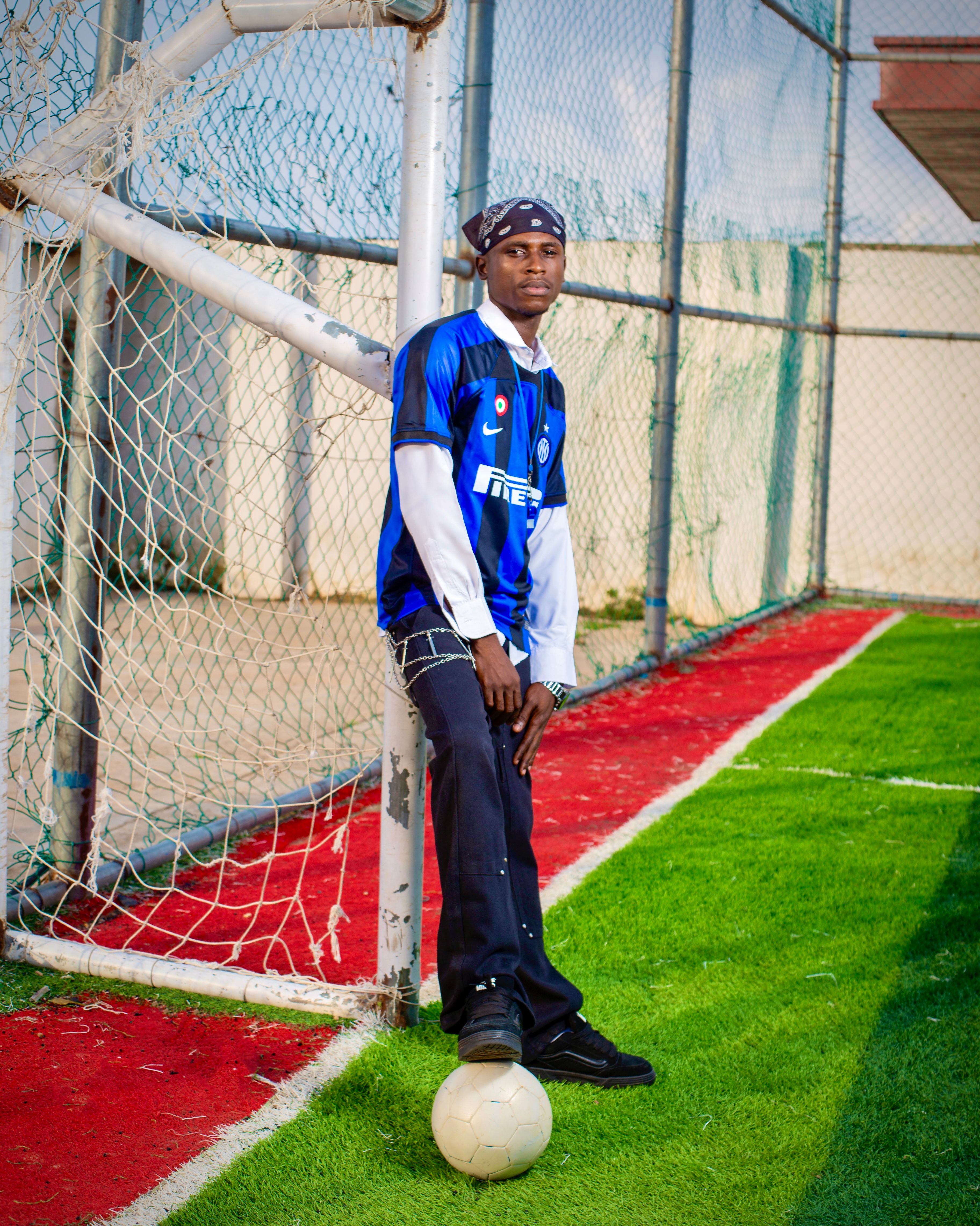 A man in football gear poses by a goal post on an artificial soccer field.