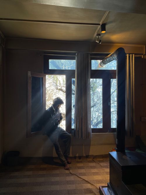 Free A person enjoying a warm beverage by the window with sunrays streaming in, during a winter morning indoors. Stock Photo