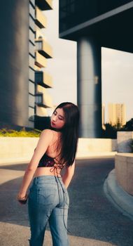 Stylish young woman posing outdoors with modern architecture in the background, captured at sunset.