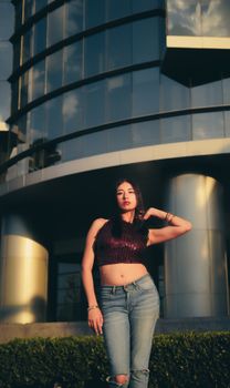 Stylish young woman posing confidently in front of a modern glass building during the day.