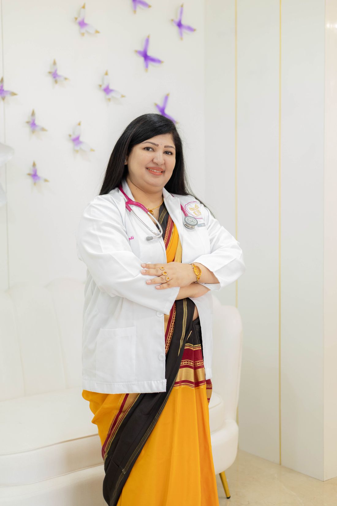 A smiling doctor in a saree and white coat