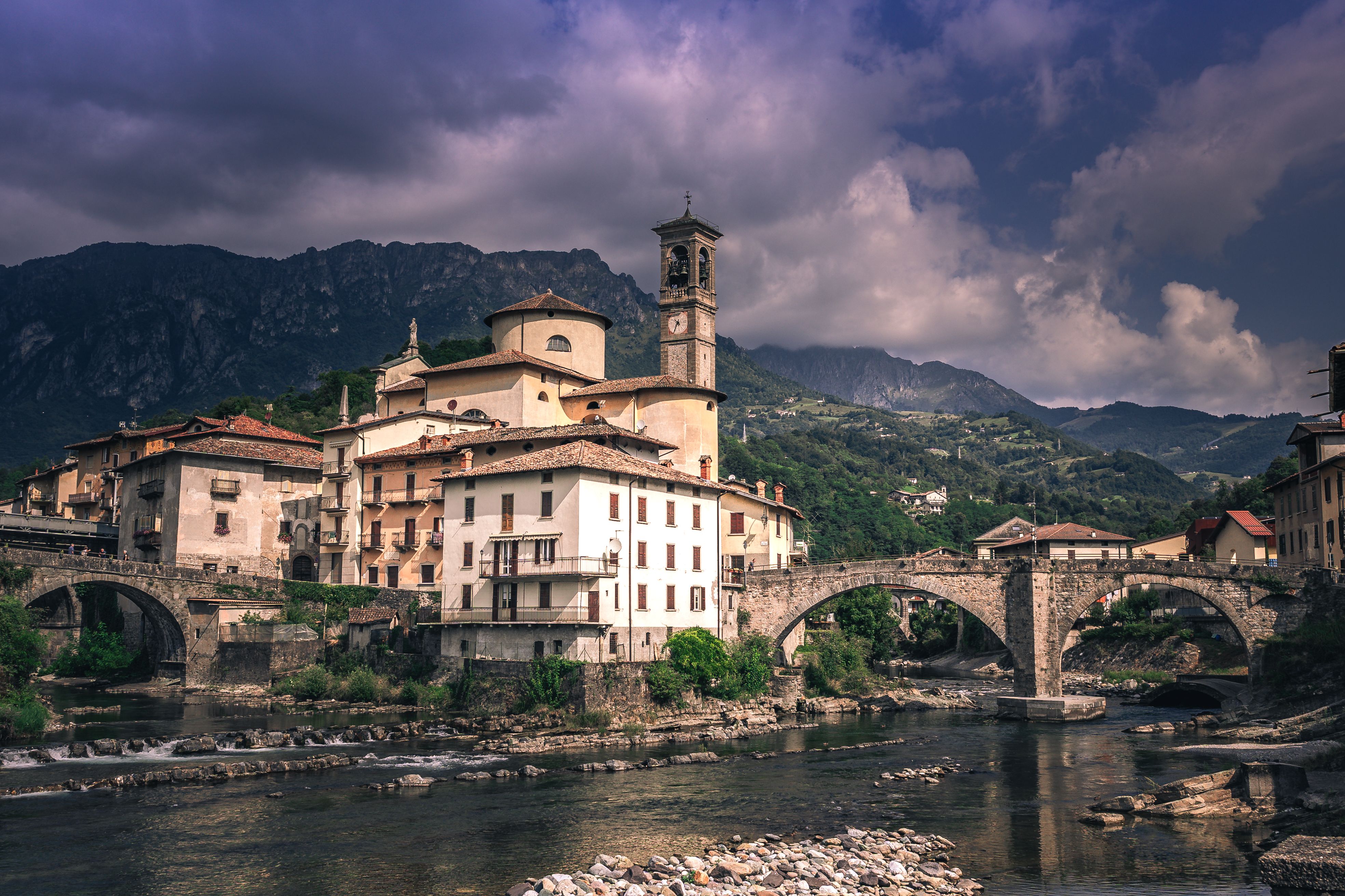 Charming village scene in Italy with mountains, stone bridge, and historic architecture.