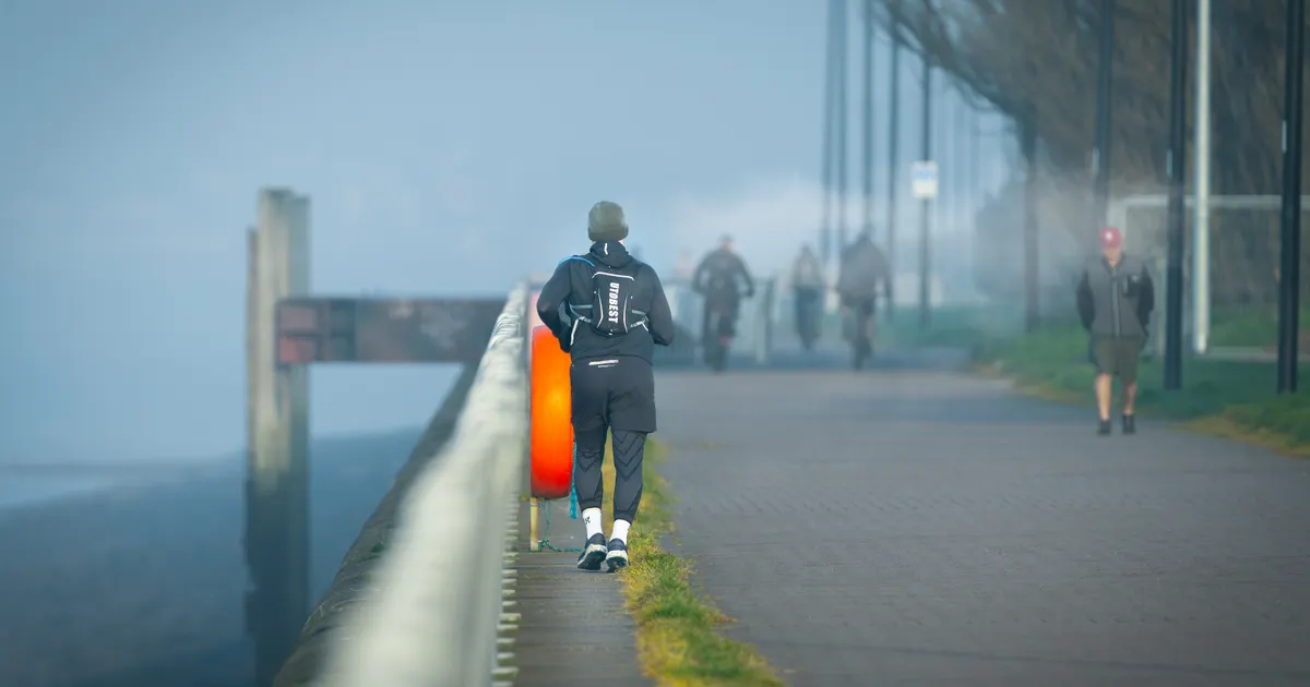 People walking and jogging along a foggy waterfront path