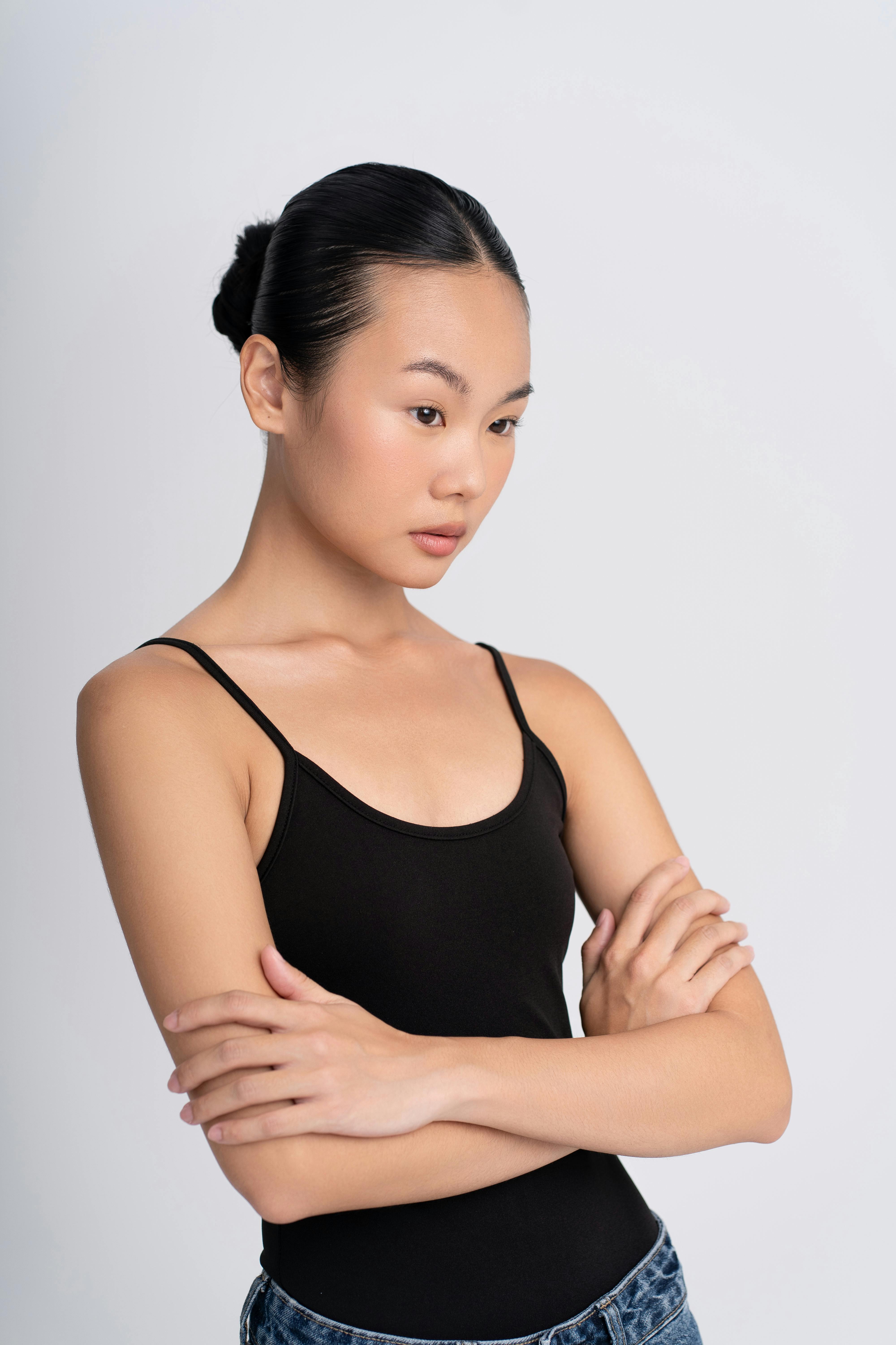 Young woman in black top with arms crossed, looking contemplative against neutral background.