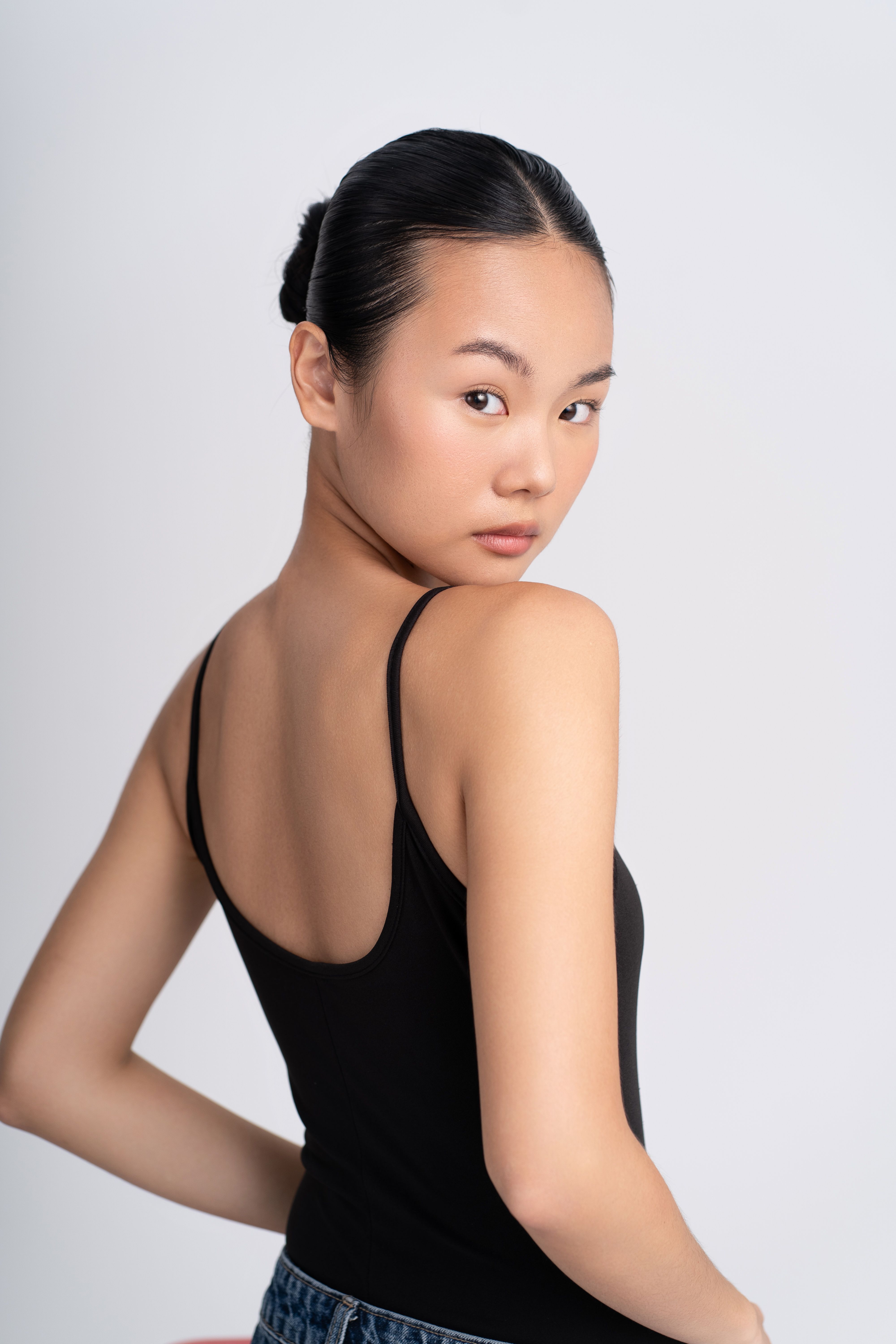 Striking portrait of a young woman wearing a black tank top, looking confidently over her shoulder.