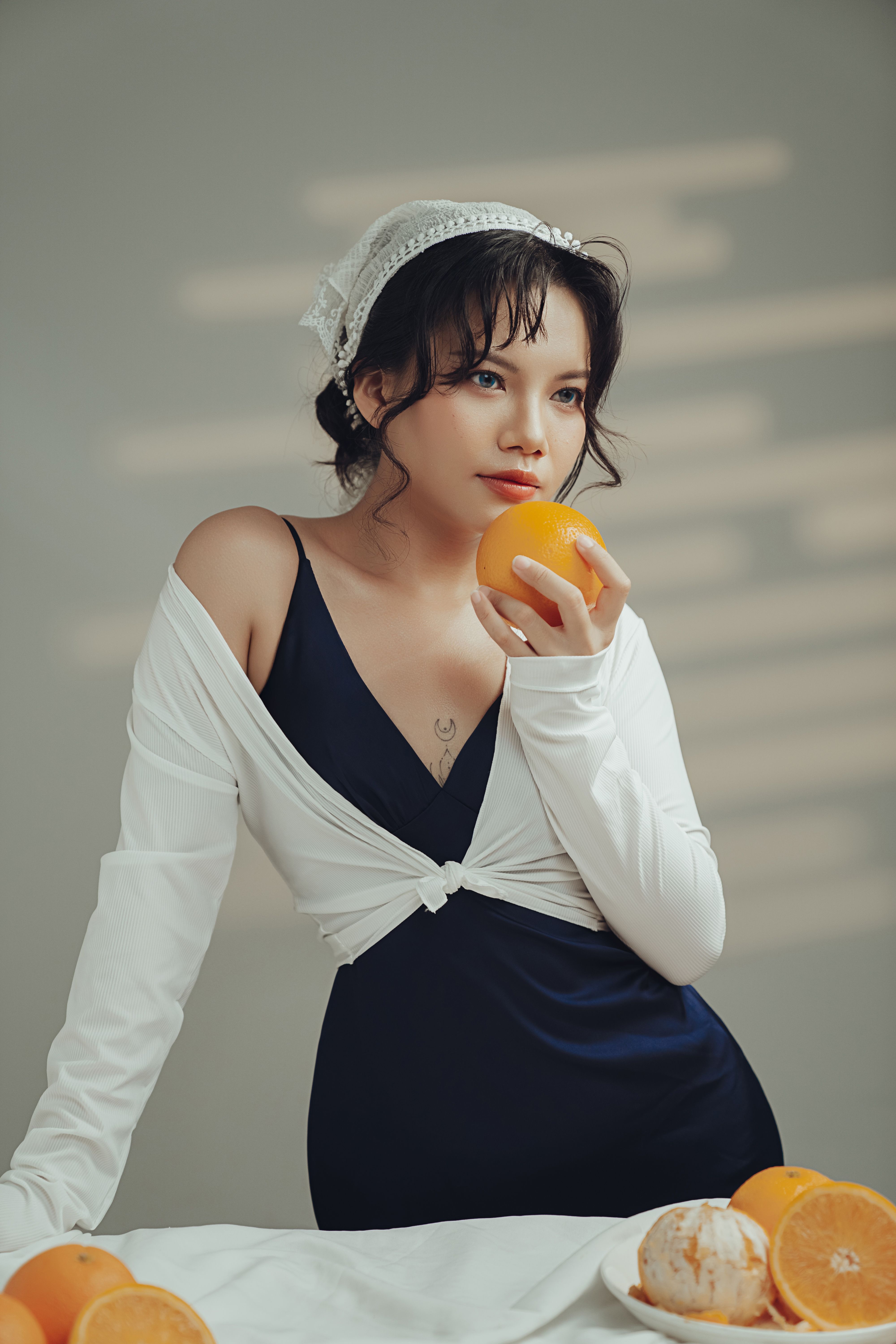 Stylish woman in elegant attire holding an orange, creating a sophisticated indoor scene.
