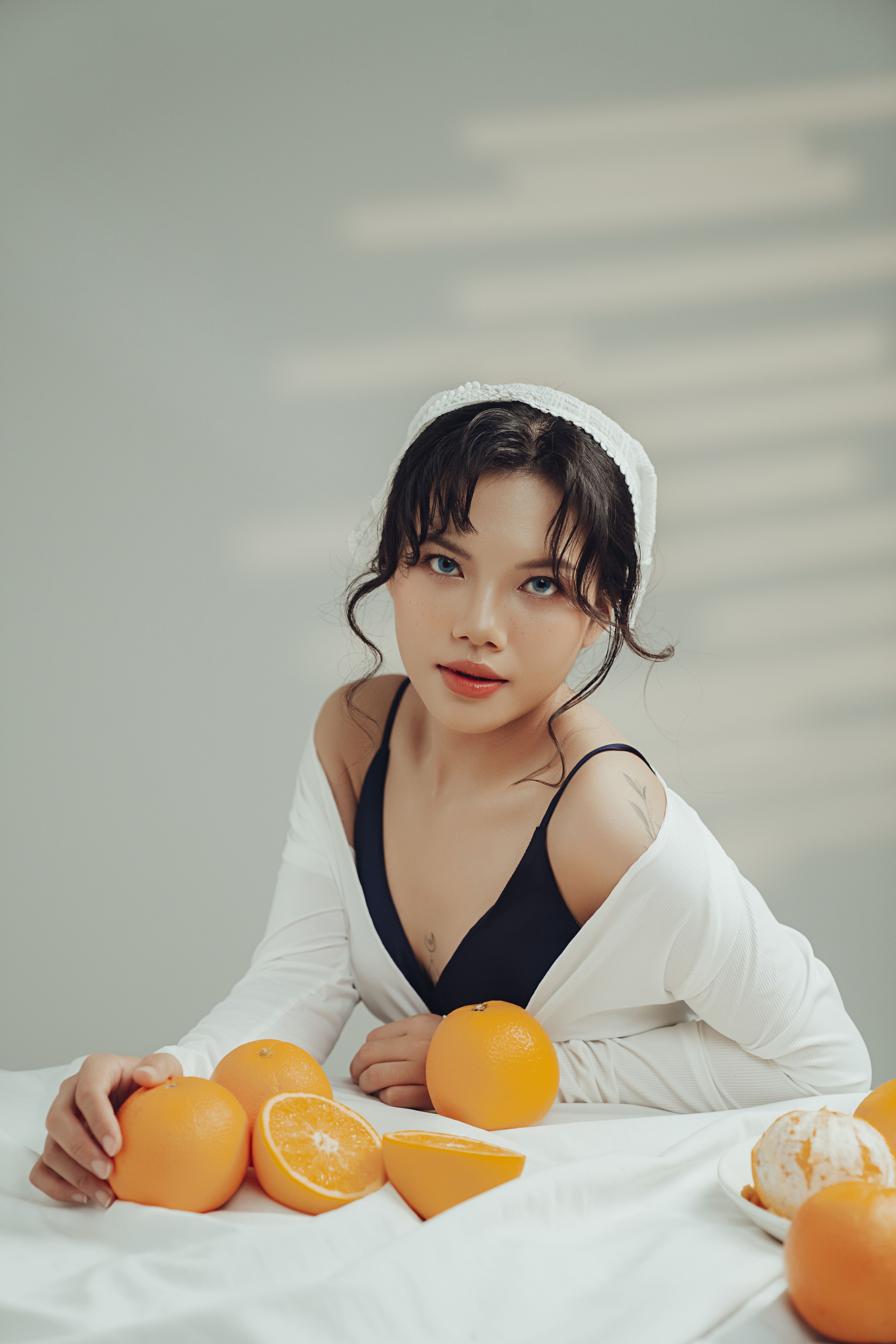 Elegant young woman posing with oranges in a serene minimalist space.