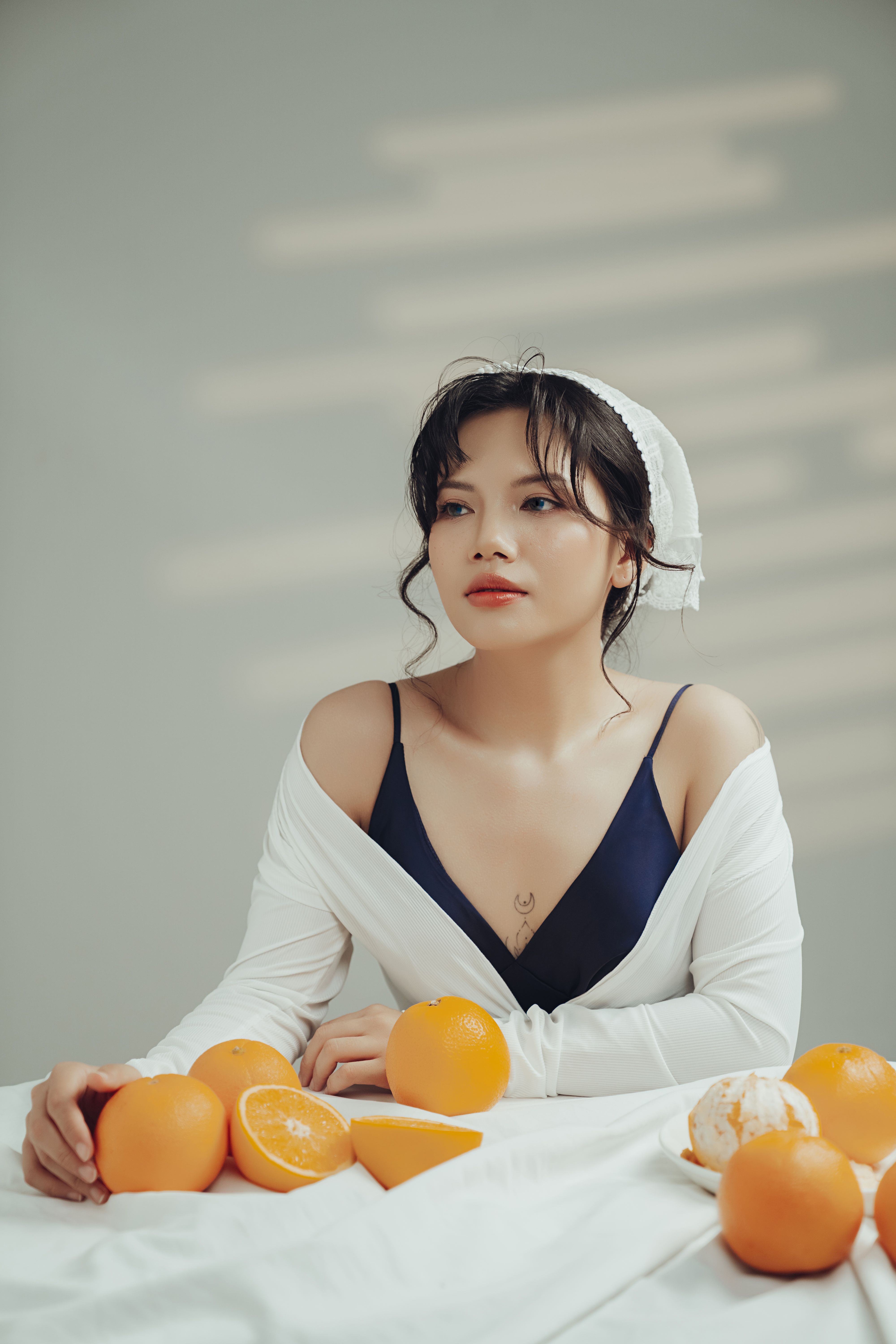 Elegant woman sitting at table with fresh oranges, creating a serene and fresh mood.
