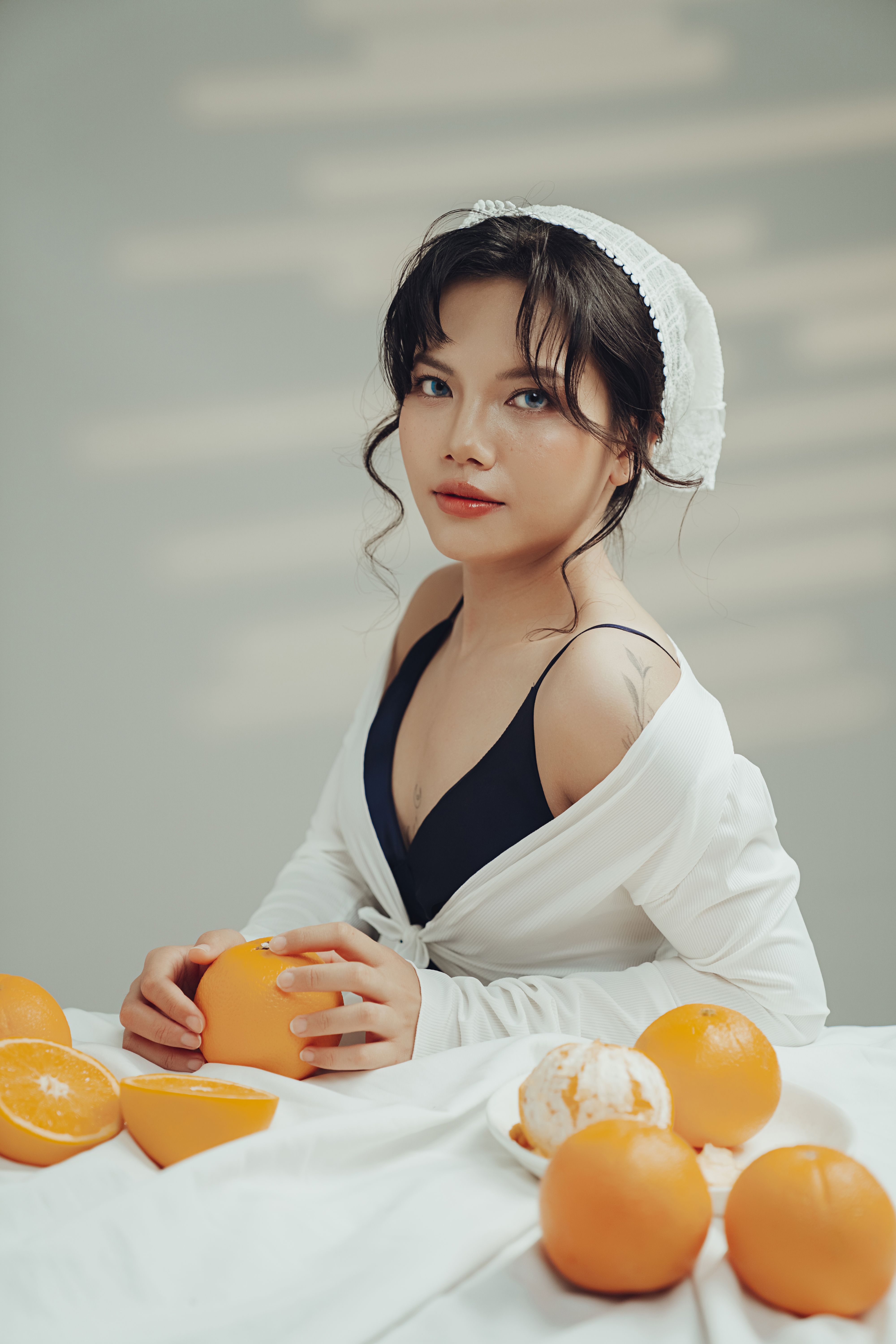 Stylish woman in white posing with fresh oranges on a table indoors.