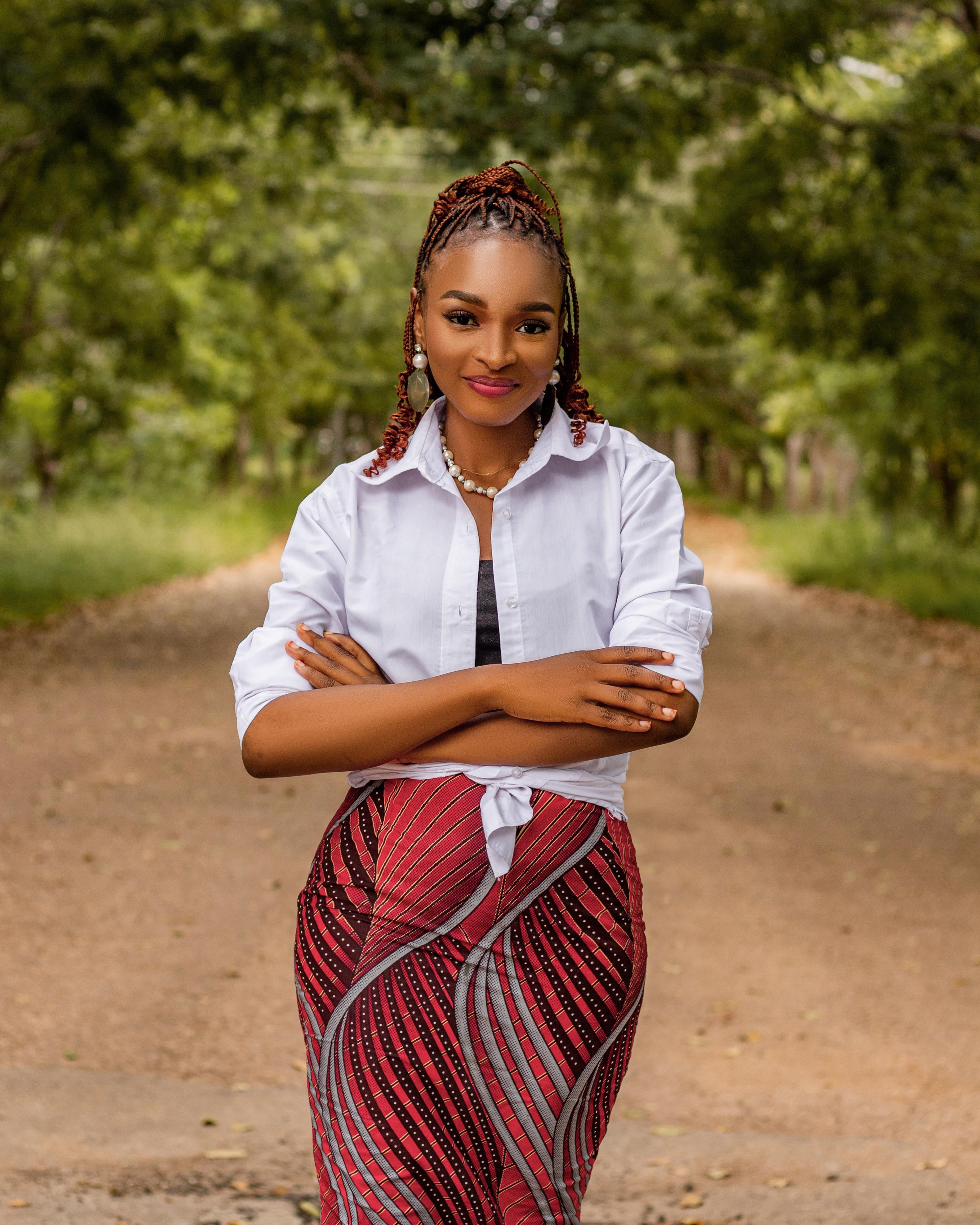 A confident young woman stands on a serene tree-lined path, exuding strength and poise.